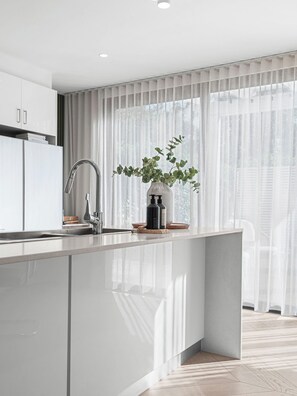 A modern kitchen with a large island, stainless steel appliances, and a view of the outdoors through sheer curtains.