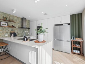 A modern kitchen with white cabinetry, a central island, a built-in stove, and a refrigerator.