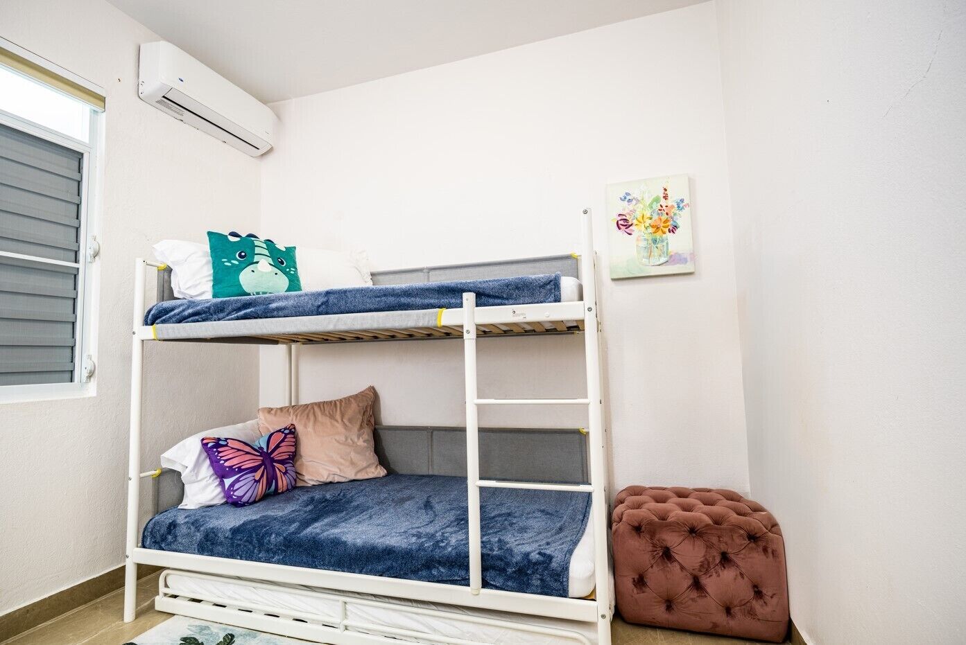 A bunk bed with a pillow, a butterfly pillow, and a small tufted ottoman.