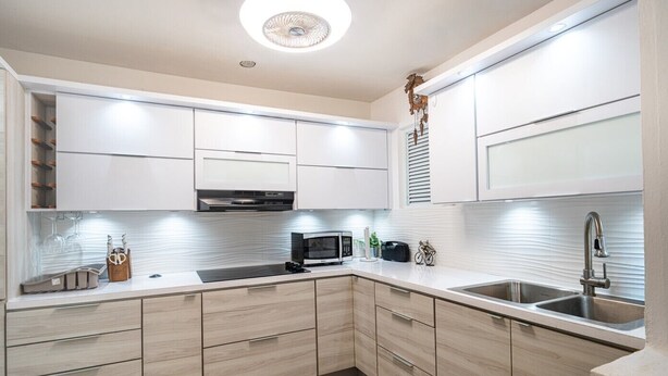 A modern kitchen with white cabinets, a microwave, a sink, and a decorative clock.