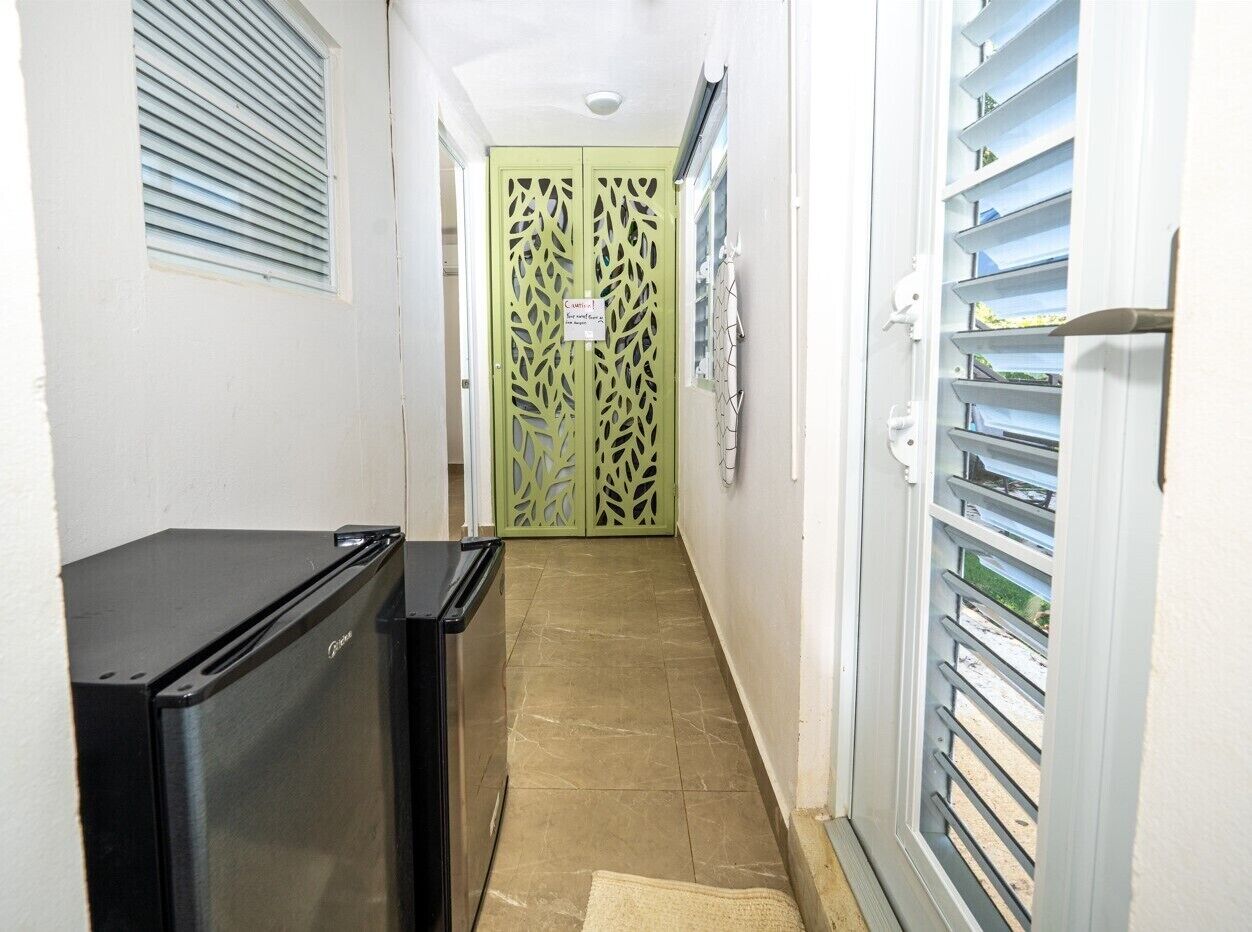 A narrow hallway with a refrigerator, a green door, and a window with blinds.