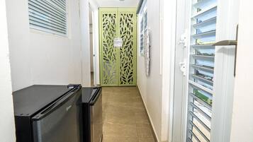 A narrow hallway with a refrigerator, a green door, and a window with blinds.