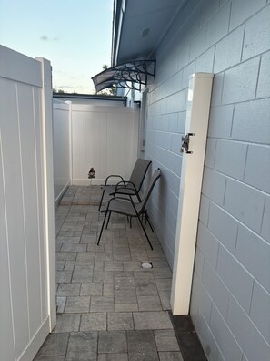 Un espace patio agrémenté d’une clôture blanche, d’un coin salon abrité et d’un climatiseur fixé au mur.