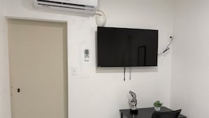 Habitació amb porta tancada, aire condicionat fixat a la paret, televisió de pantalla plana, taula petita amb cadira i una planta en test.