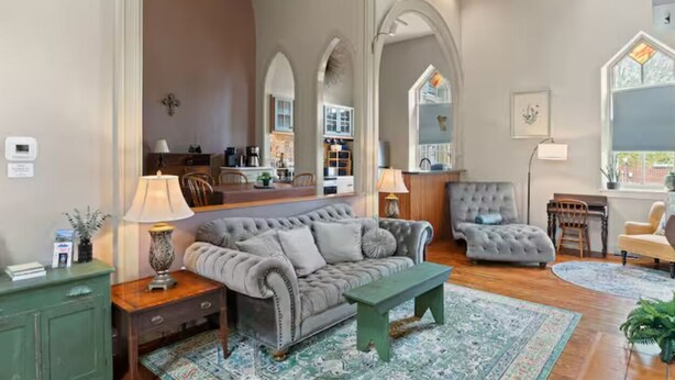 Un salón amplio con un sofá grande, un sillón más pequeño, una mesa de centro de madera y una zona de comedor con mesa y sillas.
