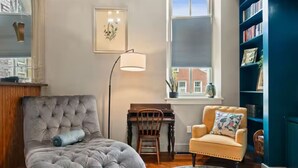 Una habitación con un sofá capitonado, un piano, una silla, una lámpara de pie, una estantería y un ventanal con vistas.