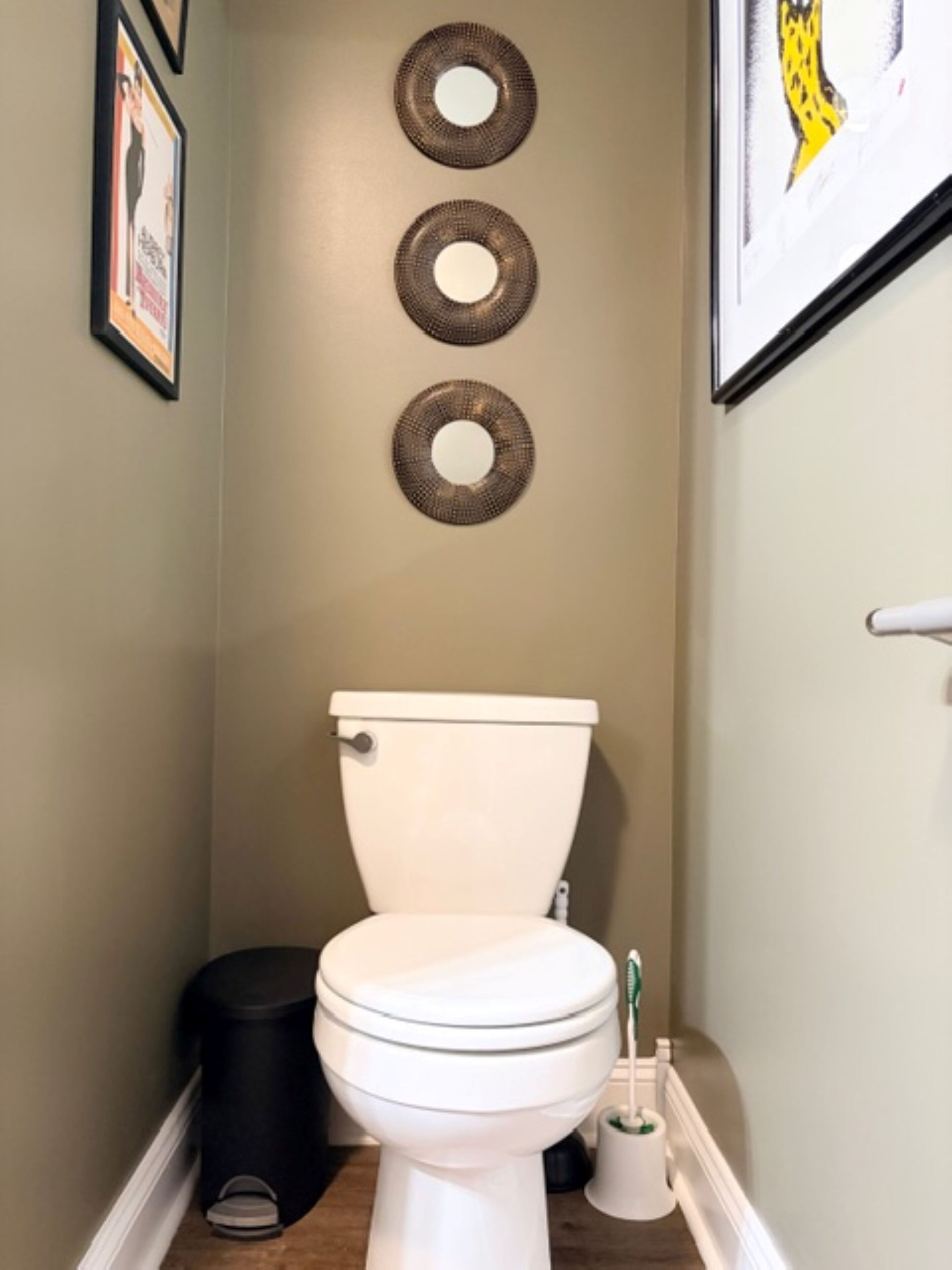 A bathroom with a toilet, a trash bin, and a toilet brush.