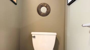 A bathroom with a toilet, a trash bin, and a toilet brush.