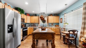 Una cocina con armarios de madera, un refrigerador de acero inoxidable, una mesa de comedor de madera y una barra para colgar ollas.