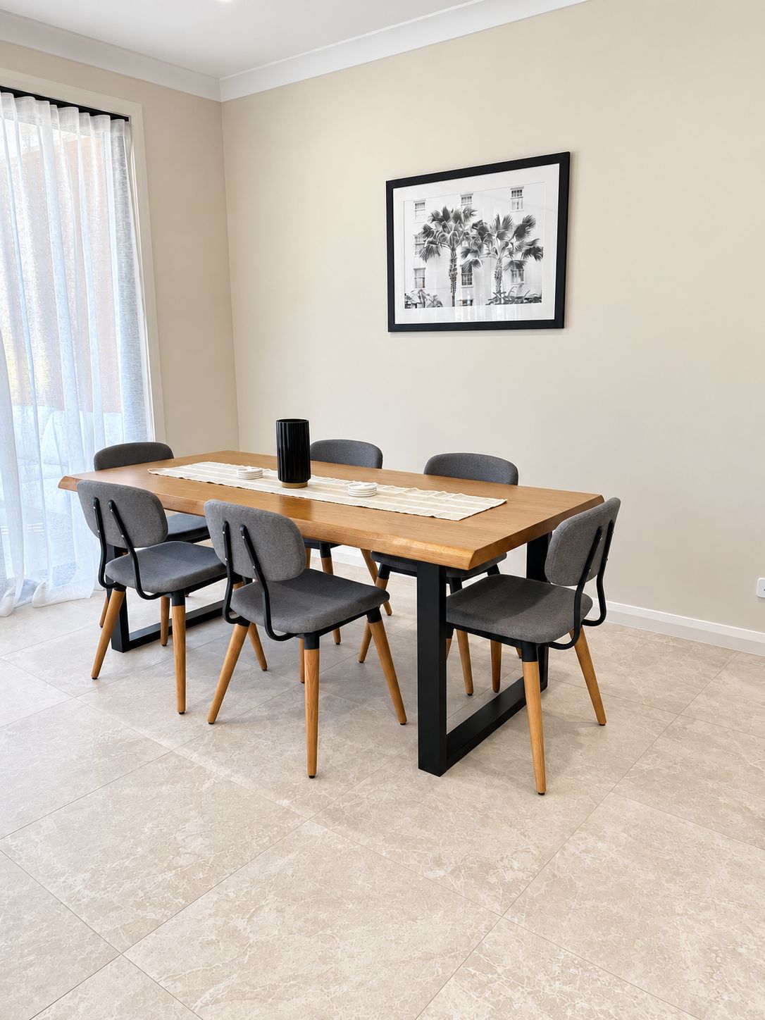 A dining area with a wooden table, six grey chairs, and a framed black and white photograph on the wall.