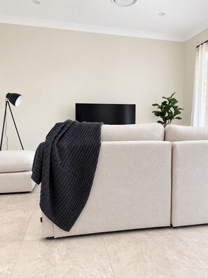 A modern living room with a sofa, a flat-screen TV, a floor lamp, and a potted plant. - STONE -  Luxury * Bay Views * Walk to Marina & Town (Nelson Bay)