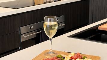 Eine moderne Küche mit Marmor-Spritzschutz, dunklen Holzschränken und einem Holzschnittbrett mit einem Glas Weißwein sowie verschiedenen Käse- und Fleischsorten.