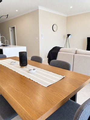 A modern living room with a wooden dining table, grey sofas, a clock on the wall, and a floor lamp. - STONE -  Luxury * Bay Views * Walk to Marina & Town (Nelson Bay)