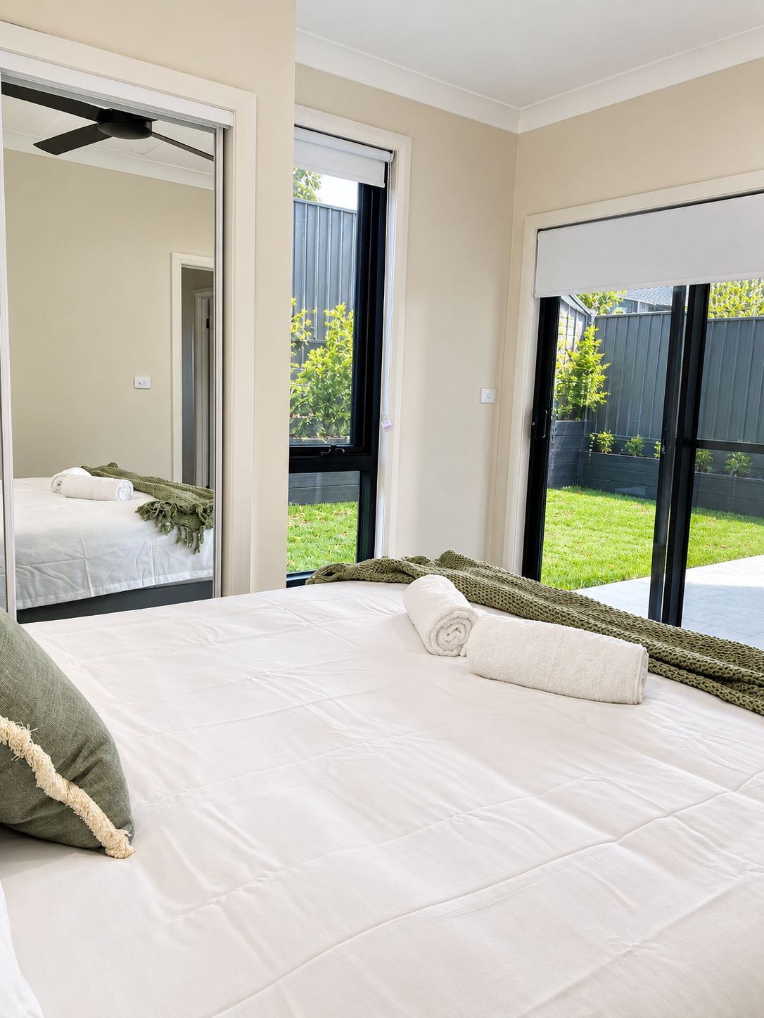 A hotel room with a bed, a window, and a view of a backyard.