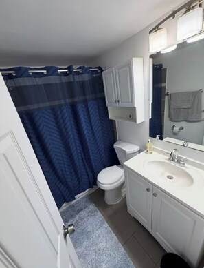 A bathroom with a white sink, a mirror, a toilet, and a shower curtain.