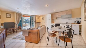 A modern living room with a sofa, TV, and dining area with chairs and a table. - Villa Montegolo, Happy Apartment (Costermano)
