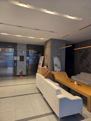 A modern lobby with a reception desk, seating area, and elevators. - Someone Hotel (Yeosu)