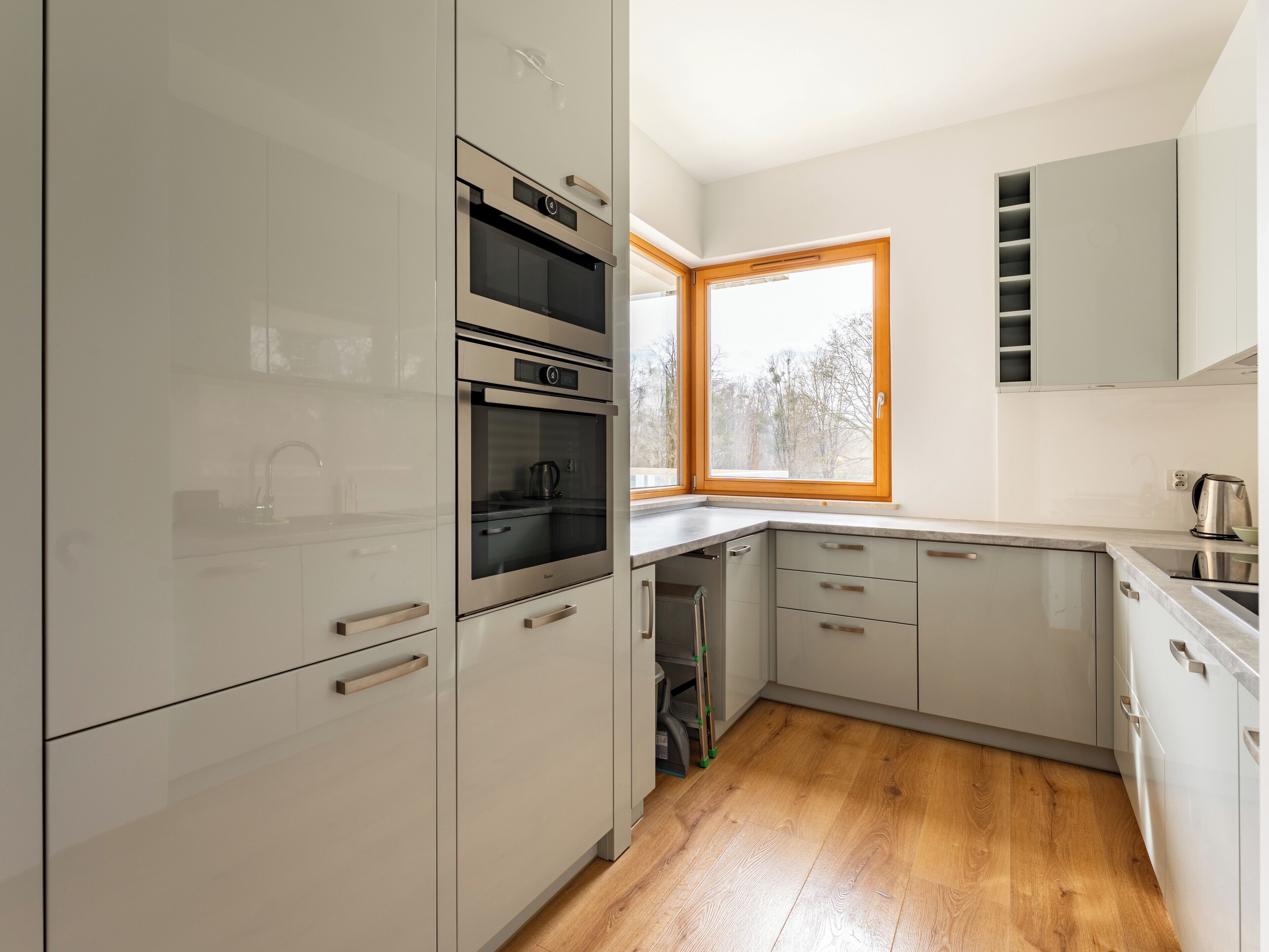 A modern kitchen with built-in appliances, a window, and wooden flooring.
