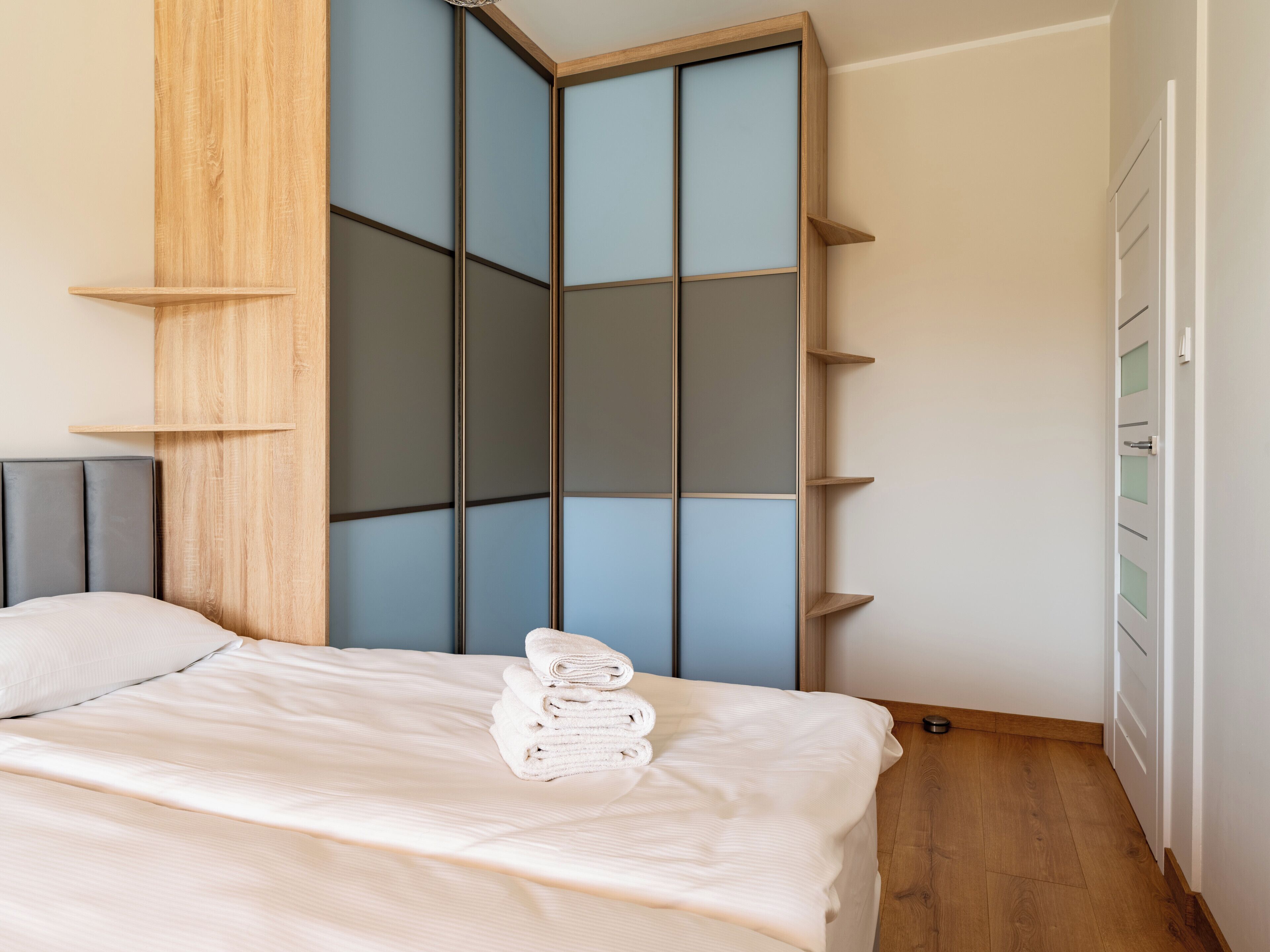 A bedroom with a bed, a wooden wardrobe, and a white door.