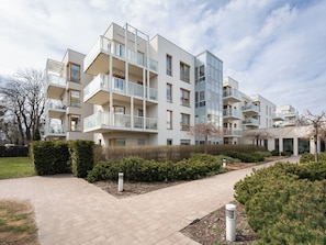 A modern multi-story residential building with balconies, a paved walkway, and landscaped greenery. - Brzeźno Coastal Comfort Apartment (Gdańsk)