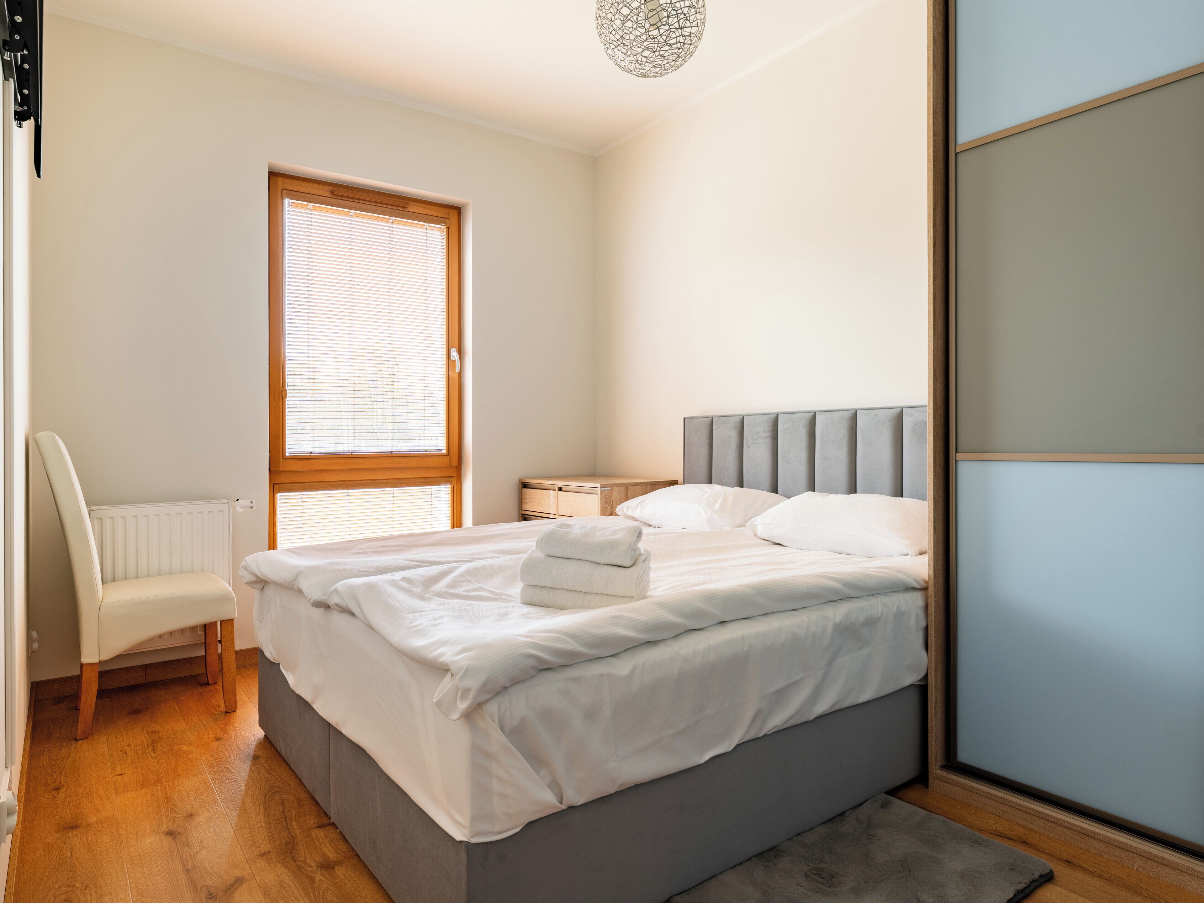 Une chambre à coucher comprenant un lit, une chaise, une table de chevet et une fenêtre avec des stores.