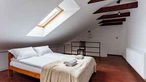 Ein Schlafzimmer mit schrägen Wänden, einem Oberlicht, einem Bett mit weißer Bettwäsche, einem Sessel und einer Heizung.