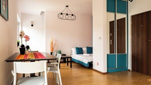 Ein modernes Zimmer mit Holzboden, einem Esstisch mit Stühlen, einem Bett mit blauen Akzenten und einem Kleiderschrank.