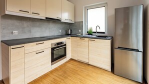 Eine moderne Küche mit hellen Holzschränken, einem Edelstahlkühlschrank, einem Einbauofen und einem Fenster mit Blick.