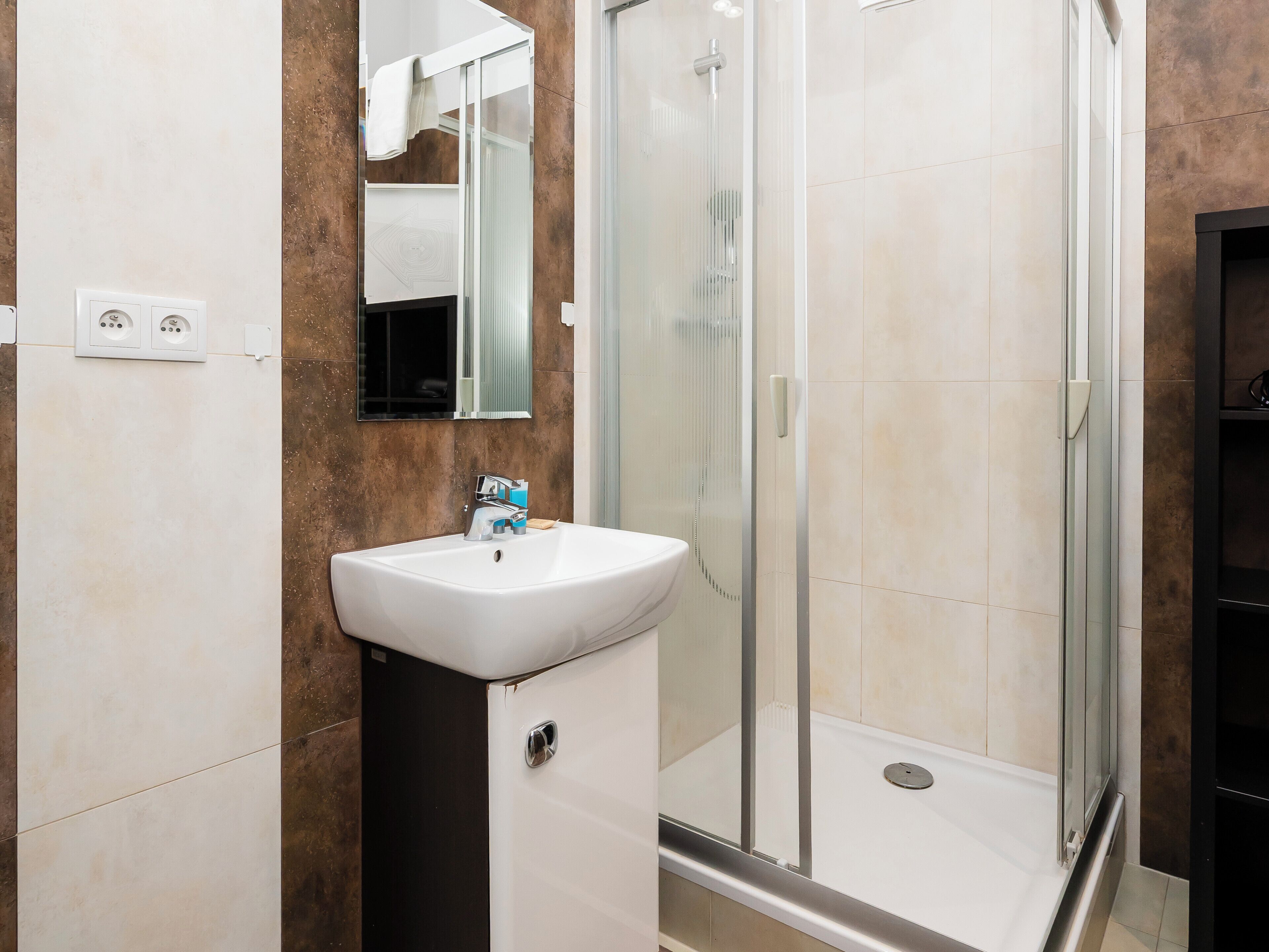 Une salle de bain avec un lavabo blanc, un miroir, une douche en verre et des toilettes.