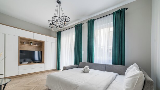 Habitació d'hotel moderna amb un llit, un televisor fixat a la paret, un sofà i una taula de menjador.