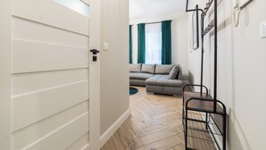 Un passadís que condueix a una zona d'estar amb un sofà, una prestatgeria de metall negre i un terra de fusta.