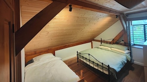 A loft bedroom with a sloped ceiling, a bed, and a window. - Wodinstead - A cosy large home in Bundanoon (Bundanoon)