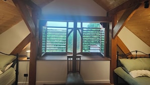 A room with a sloped ceiling, a window with wooden shutters, a bed, and a chair. - Wodinstead - A cosy large home in Bundanoon (Bundanoon)