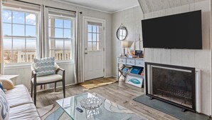 Ett vardagsrum med en öppen spis, en tv som är monterad på väggen, en fåtölj och en soffa.