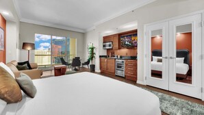 Quarto de hotel com uma cama grande, cozinha compacta, área de refeições e vista da cidade.