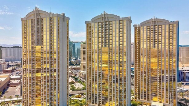 Três edifícios altos com fachada em estilo de grade, rodeados por infraestrutura urbana e áreas verdes.