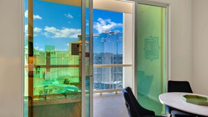 Quarto com vista para a cidade através de uma porta de vidro, uma mesa redonda e uma cadeira preta.