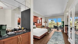 Quarto de hotel moderno com uma cama grande, uma mesa de trabalho, um espaço de refeições e vista para a paisagem urbana.