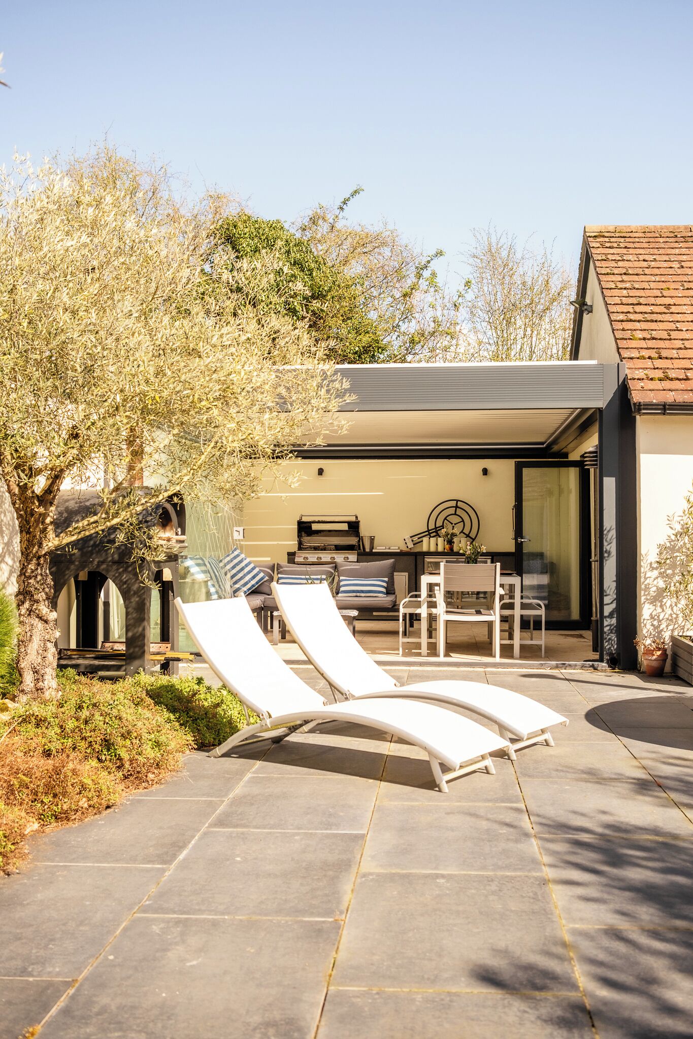 A modern outdoor patio with lounge chairs, a dining area, and a stone archway.