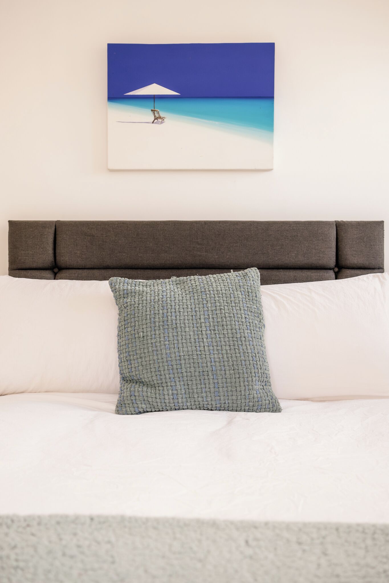 A bed with a headboard, a pillow, and a framed picture of a beach scene.