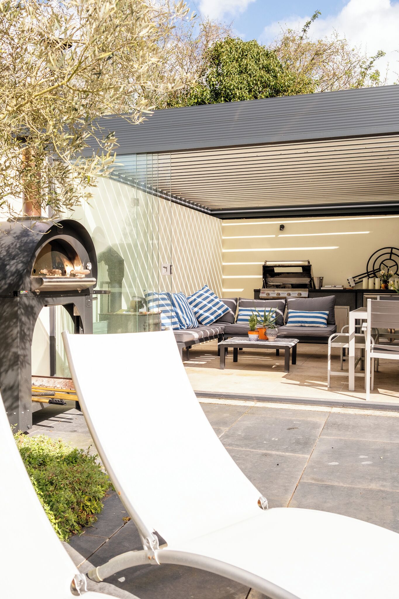 A modern outdoor patio with a stone oven, a sofa with striped cushions, and a grill area.