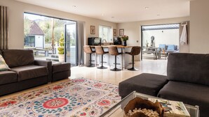 A spacious living area with a sofa, a coffee table, and a patterned rug. There is a kitchen area with bar stools and a dining table. - Stunning 1 BD Home in Worcestershire (Worcester)