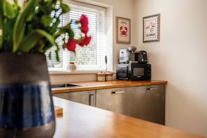 A kitchen with a microwave, coffee maker, and a window with blinds.