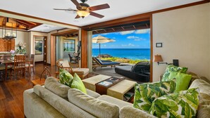 A spacious living area with a view of the ocean, a ceiling fan, and a dining area with wooden furniture. - Honu Kai Villa 1 by Alekona Kauai: Luxury 3BR Oceanfront home with resort amenities (Koloa)