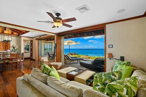 A spacious living area with a view of the ocean, a ceiling fan, and a dining area with wooden furniture. - Honu Kai Villa 1 by Alekona Kauai: Luxury 3BR Oceanfront home with resort amenities (Koloa)