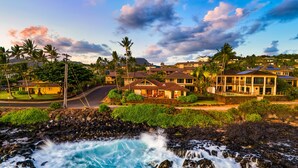 A coastal residential area with houses, a road, and a rocky shoreline with waves. - Honu Kai Villa 1 by Alekona Kauai: Luxury 3BR Oceanfront home with resort amenities (Koloa)