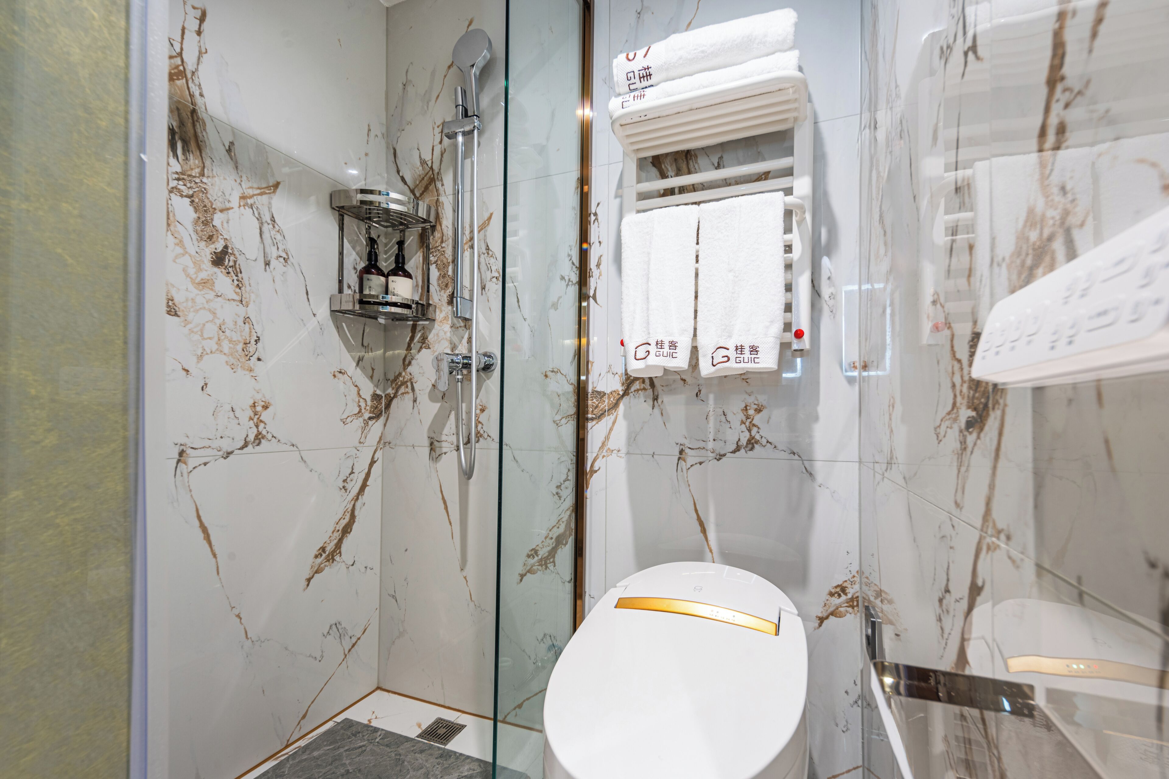 Un baño con cabina de ducha de vidrio, inodoro blanco y toallero con toallas.