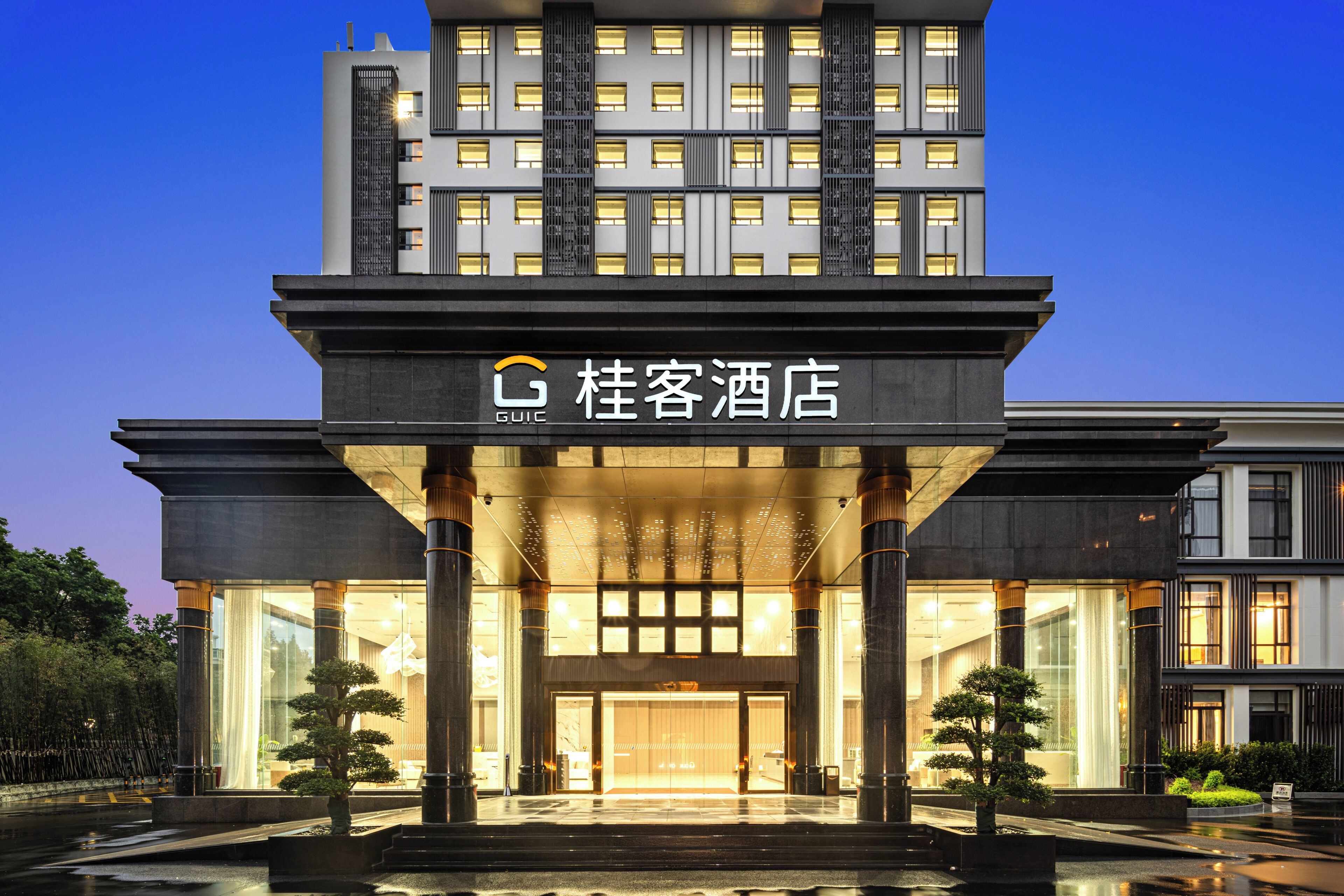 A modern hotel entrance with a large glass facade, columns, and a sign indicating the hotel name.