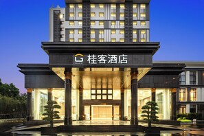 A modern hotel entrance with a large glass facade, columns, and a sign indicating the hotel name.