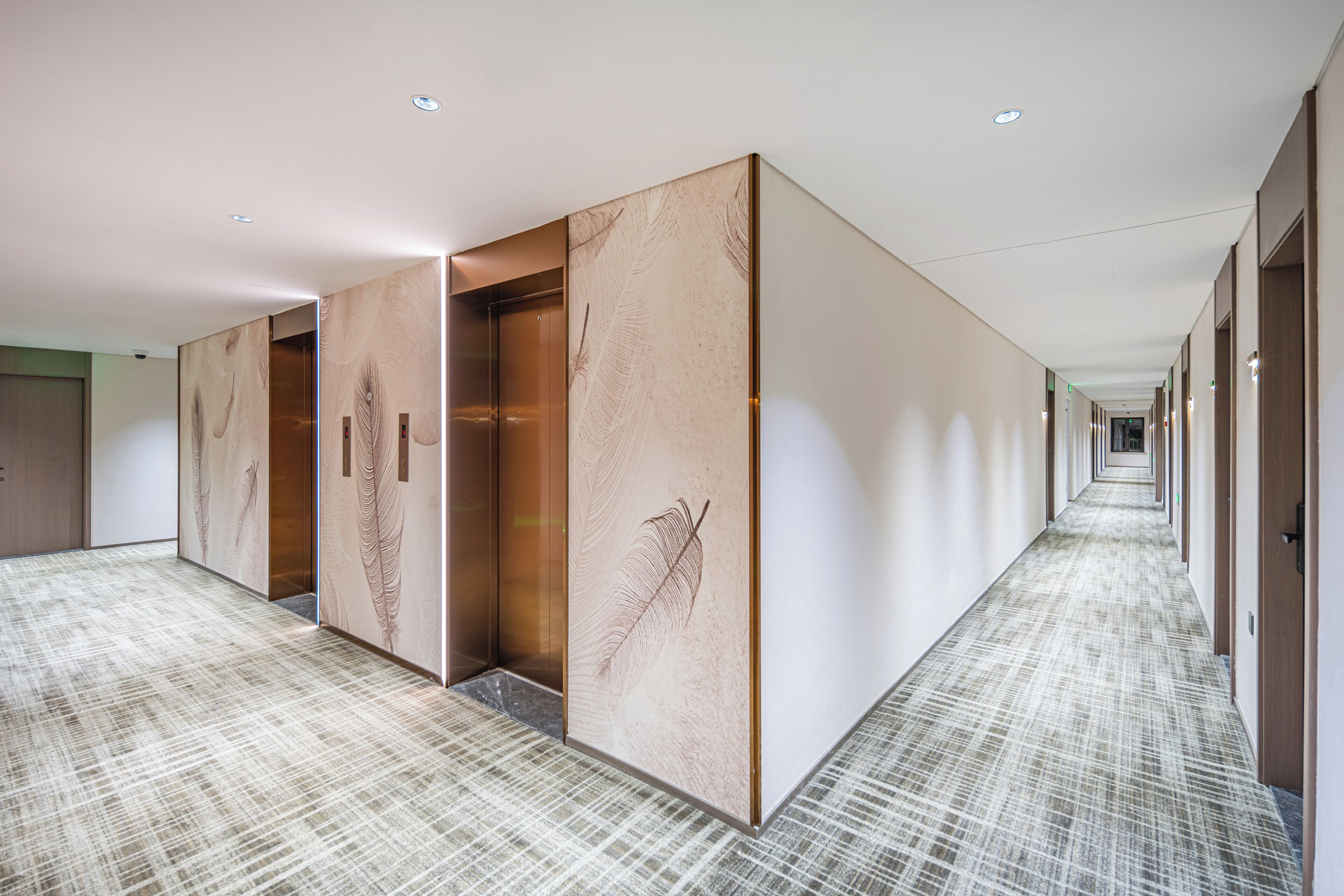 A long, narrow hotel corridor with a patterned carpet, wooden panel walls, and a series of doors.